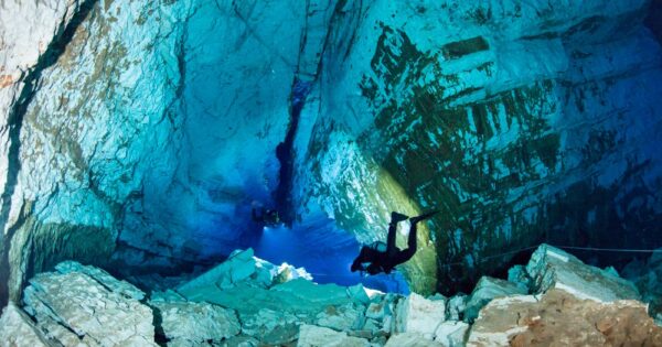 Diver in drysuit diving in cave, deep blue water